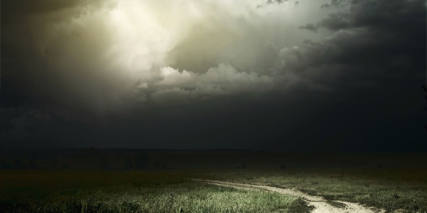 Dark storm clouds over a dirt track and grass