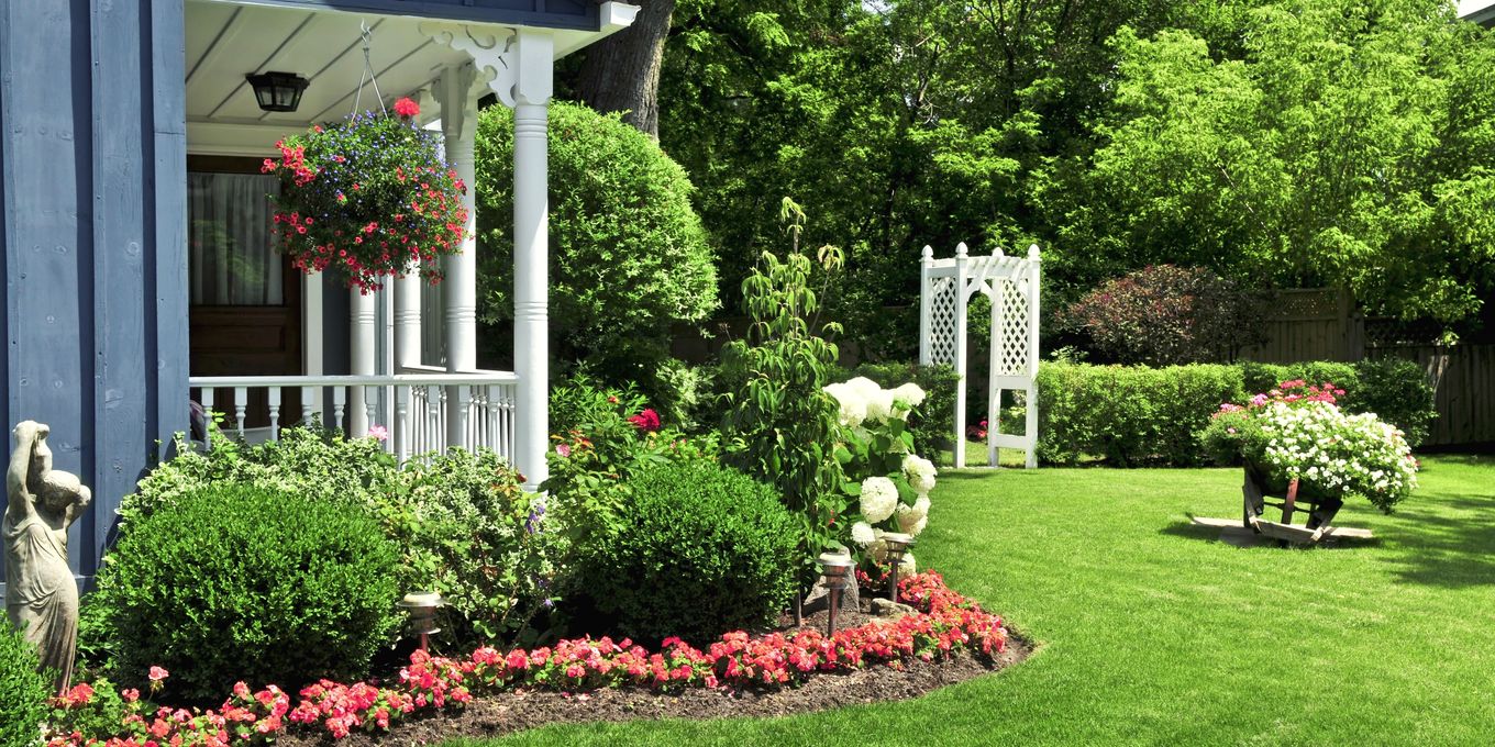A front yard with a green lawn, shrubs and a bed of red flowers